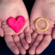 infezioni sessuali. aids/hiv. due palmi delle mani: uno contiene un preservativo, l'altro un cuore
