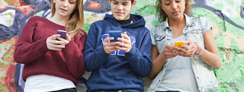 social: tre ragazzi con lo smartphone seduti su un muretto