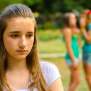 violenza e abusi, una giovane ragazza cammina con il volto triste e sullo sfondo due ragazze parlano tra loro