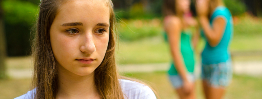 violenza e abusi, una giovane ragazza cammina con il volto triste e sullo sfondo due ragazze parlano tra loro