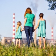 aria inquinata: una donna di spalle mentre tiene per mano due bambine, all'orizzonte i fumi di una fabbrica