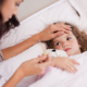 isindromi simil-influenzali, una bambina a letto mostra sintomi simil influenzali e la madre al suo capezzale le misura la febbre.