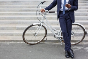  un uomo in giacca e cravatta con una bici scrive al cellulare appoggiato ad una bici