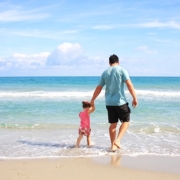 mare, un papà tiene per mano la figlia e passeggiano sulla spiaggia