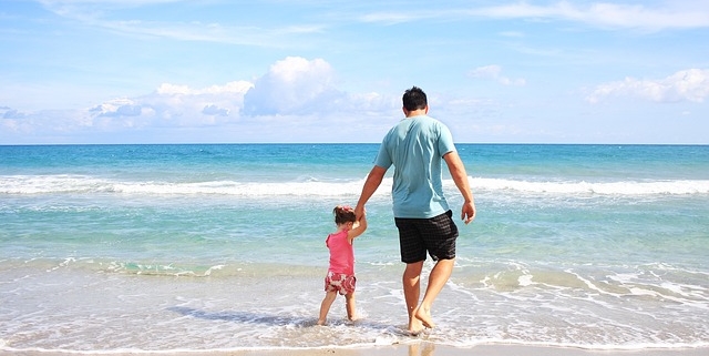 mare, un papà tiene per mano la figlia e passeggiano sulla spiaggia