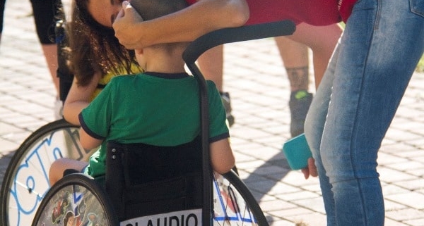 sma, bimbo sulla sedia a rotelle di spalle viene abbracciato da una donna in piedi