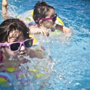 occhi, due bimbi nuotano in piscina con gli occhiali da sole e il salvagente