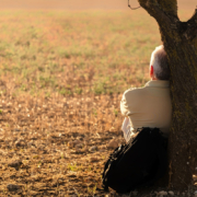 alzheimer,demenze, un uomo di spalle seduto appoggiato su un albero