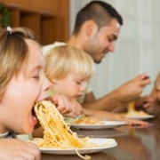 cibo condiviso a tavola in famiglia: due bimbi mangiano spaghetti con i genitori