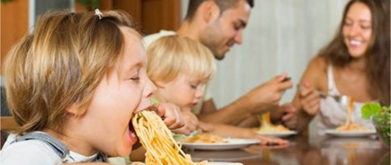 cibo condiviso a tavola in famiglia: due bimbi mangiano spaghetti con i genitori