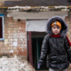 giornata mondiale infanzia, una bimba con alle spalle la casa distrutta dalla guerra in ucraina