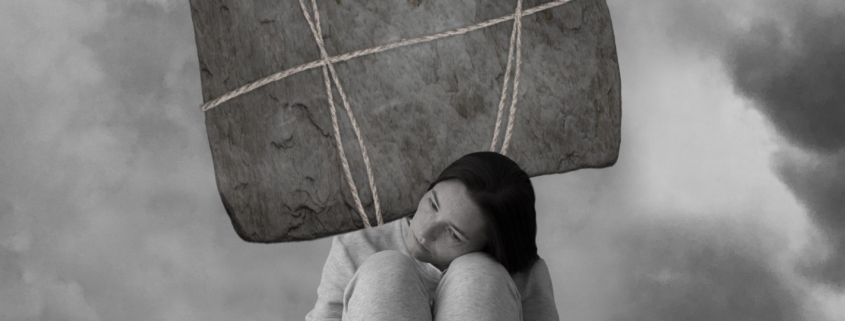 depressione, immagine in bianco e nero di una donna accovacciata, sopra la sua testa pende un grande masso