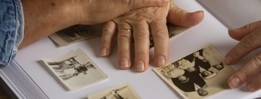 alzheimer, le mani di due anziani mentre sfogliano un album di foto in bianco e nero