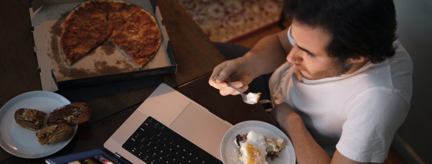 diabete, un uomo mangia di notte davanti al computer, ha una pizza tagliata a spicchi accanto e un piatto