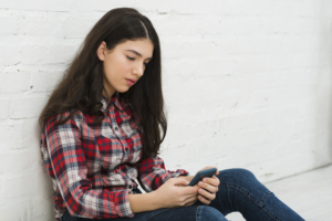 dipendenza salute mentale, una donna seduta su una superficie bianca che guarda un cellulare