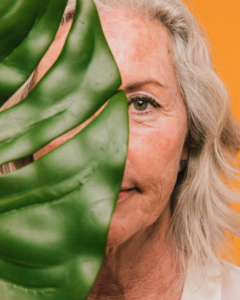 invecchiamento della pelle: una donna con i capelli bianchi con metà volto coperto da una grande foglia verde