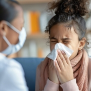 malattie respiratorie, una bambina si soffia il naso e un medico con la mascherina la visita