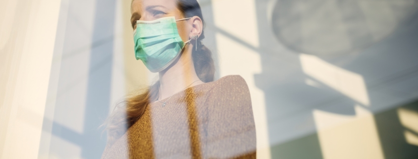 una giovane donna dietro ad un vetro indossa una mascherina