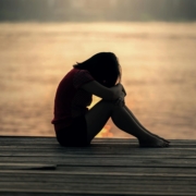 a woman sitting alone on a wooden dock by the lake, showing solitude and reflection.